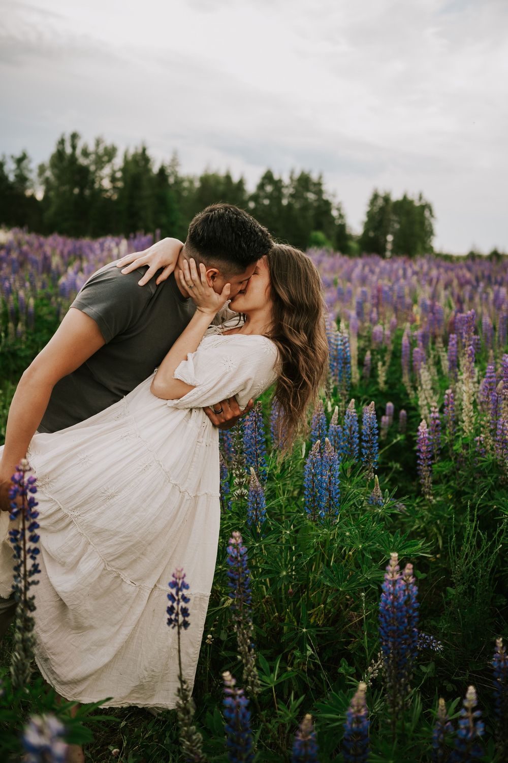 Fun and romantic photoshoot of couple dip kissing in lupine wildflower field Vancouver Island adventure Photographer