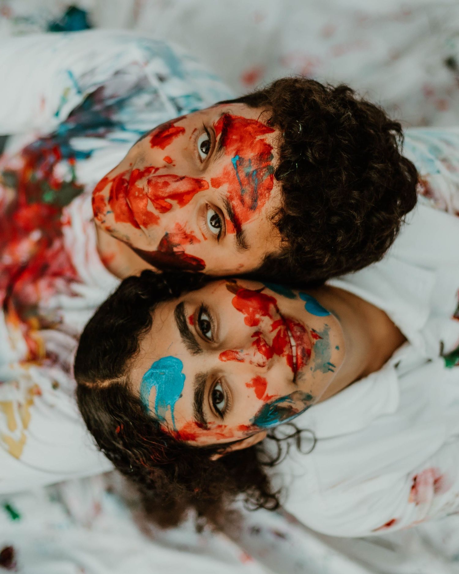 Artistic portrait of someone with splashes of red and blue paint on their face against white background. Unique engagement photoshoot.