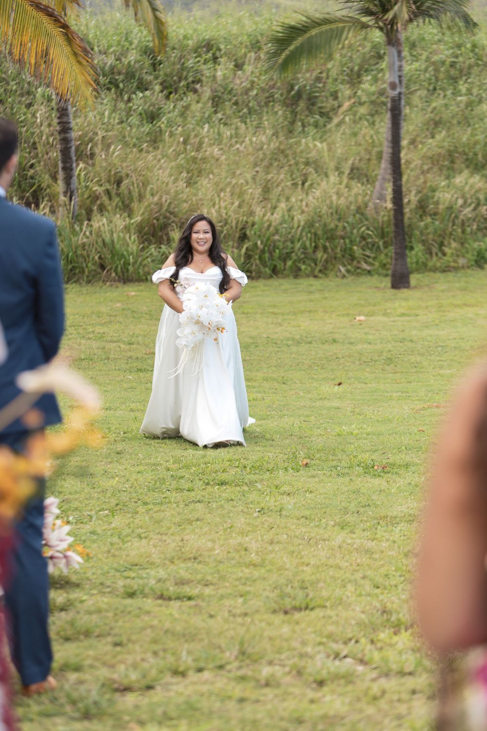 A joyful wedding celebration takes place on a grassy lawn with palm trees and tropical foliage in the background.