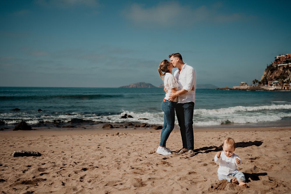 Padres besándose mientras el bebé juega con la arena (photographer in Mazatlán)