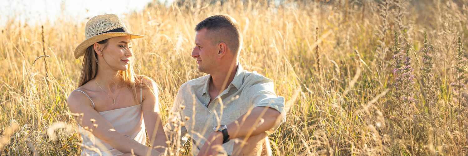 Romantyczna para siedzi razem na oświetlonym słońcem złotym polu pszenicy, ubrana w codzienne, letnie stroje.