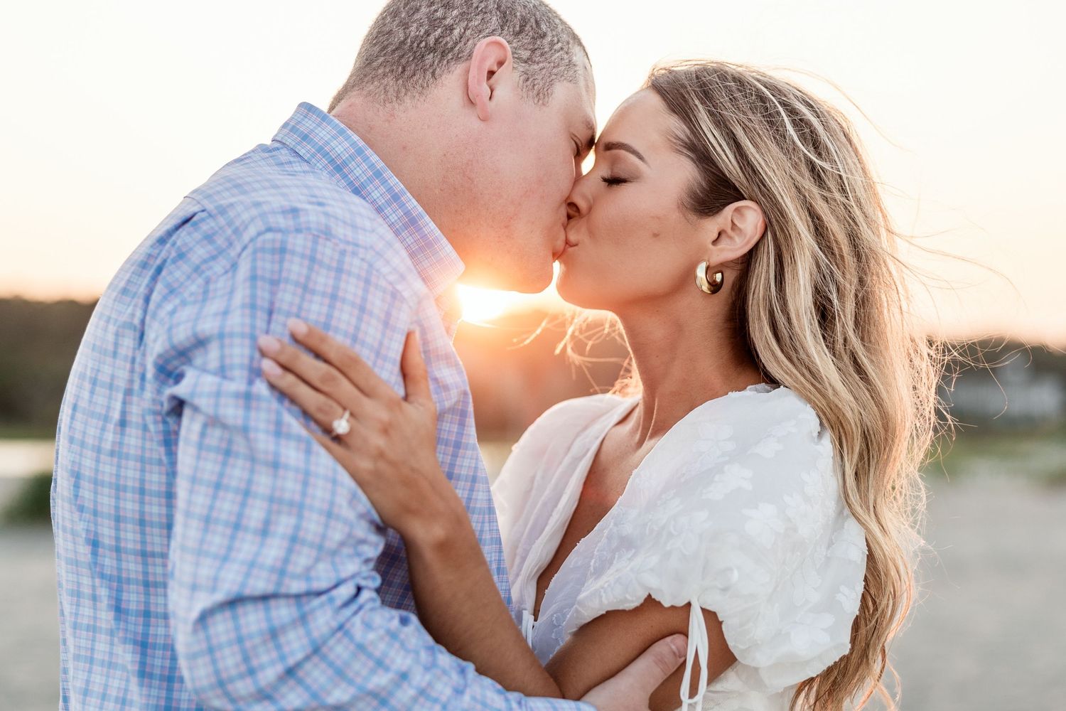 A romantic couple shares tender kisses at sunset in a natural outdoor setting.
