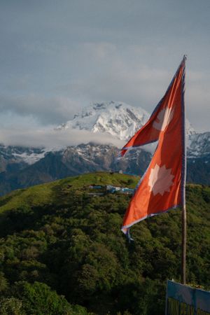 Swiss flag waves proudly against a backdrop of snow-capped Alps and green hillsides on a cloudy day.
