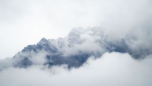Misty mountain peaks partially obscured by rolling clouds in the high Alps.