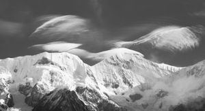 Black and white panorama of snow-covered mountain peaks against a dramatic sky.