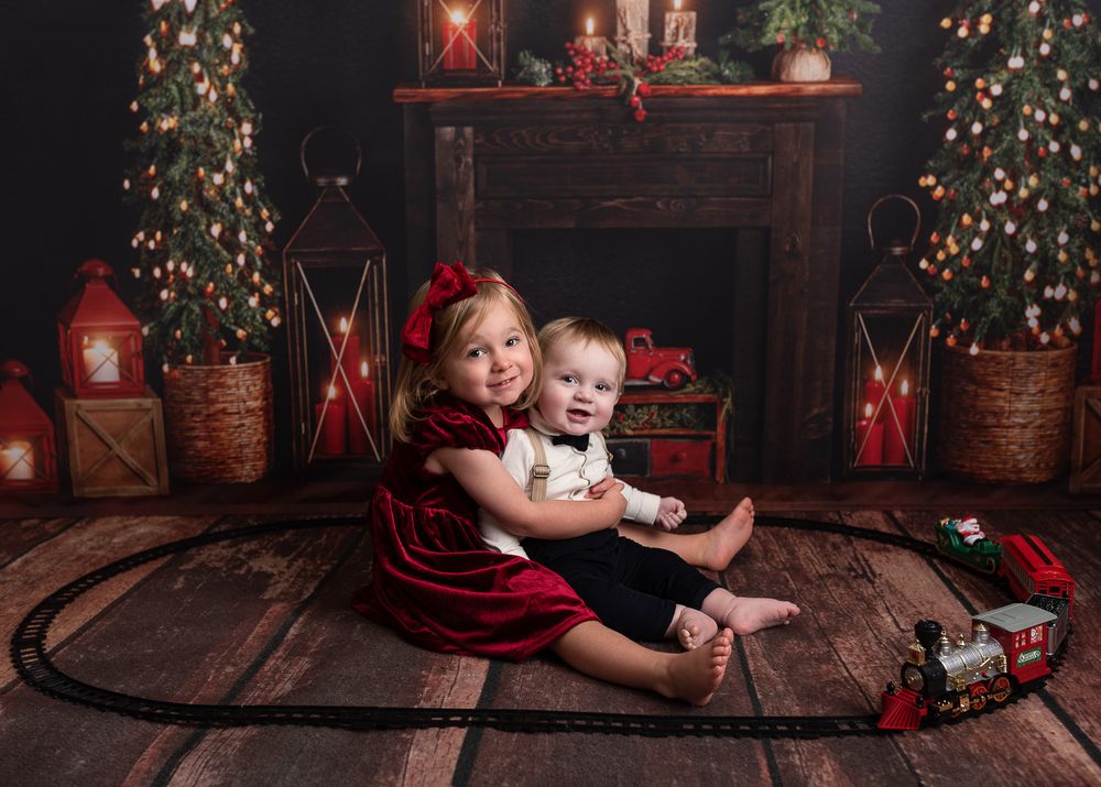 Children lying on wooden floor near decorated Christmas tree with red lanterns and festive holiday decor.