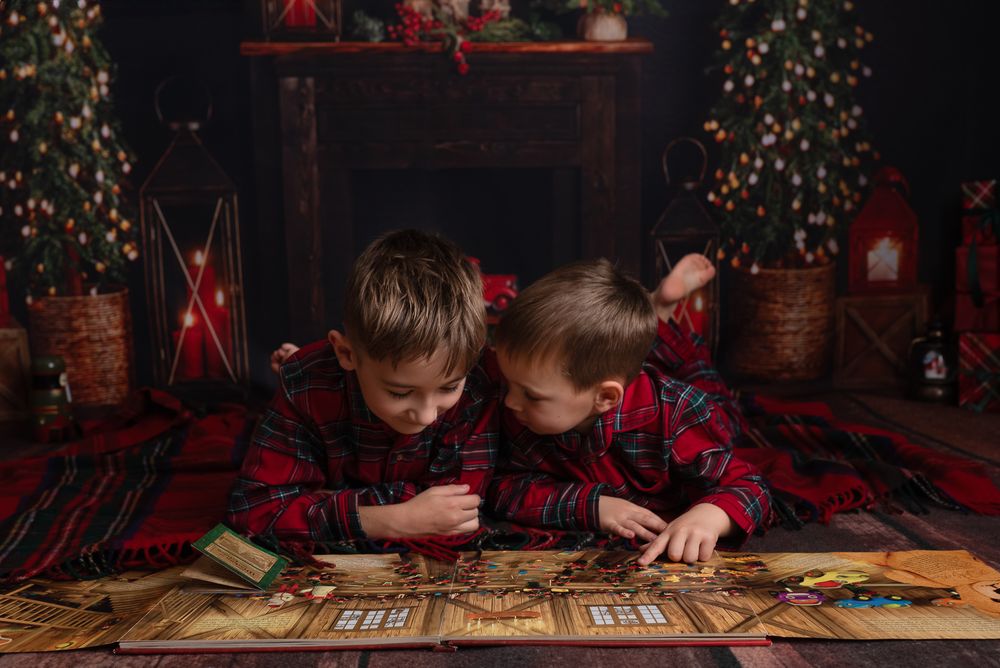 Two children play a board game together in front of a Christmas tree with twinkling lights in the background.