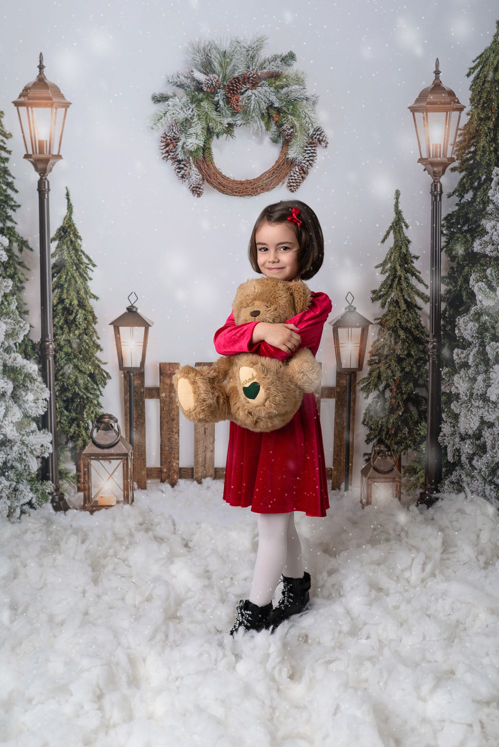 A festive winter photo setup with snow, lanterns, and holiday decorations against a light backdrop.