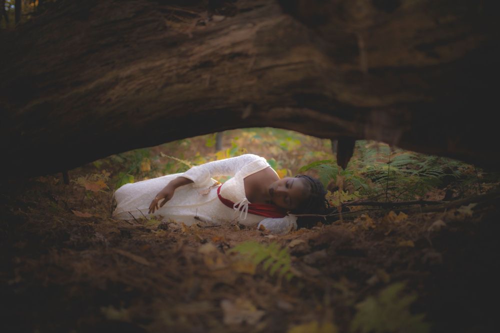 Figure in white dress lying peacefully on mossy forest ground in dreamy natural light.