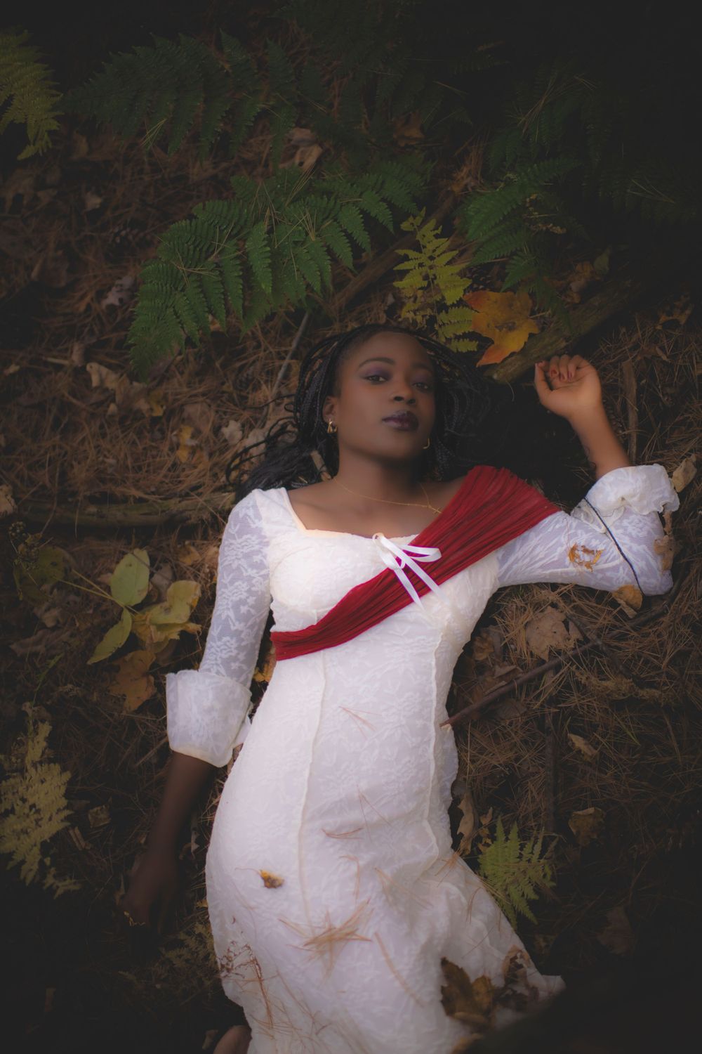 Dreamy forest scene with figure in vintage white dress lying among autumn leaves and ferns.