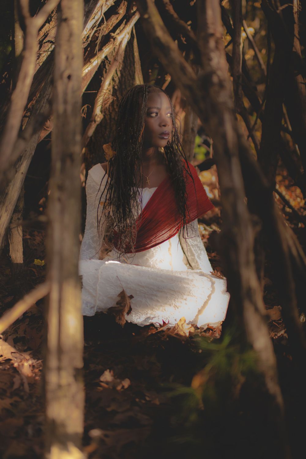 Ethereal portrait in forest featuring white dress and red wrap against autumn foliage.