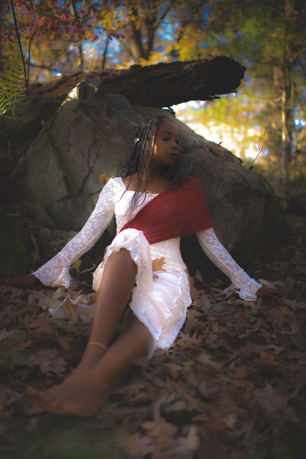 Dreamy forest scene with flowing white dress and red accent against rocky backdrop.