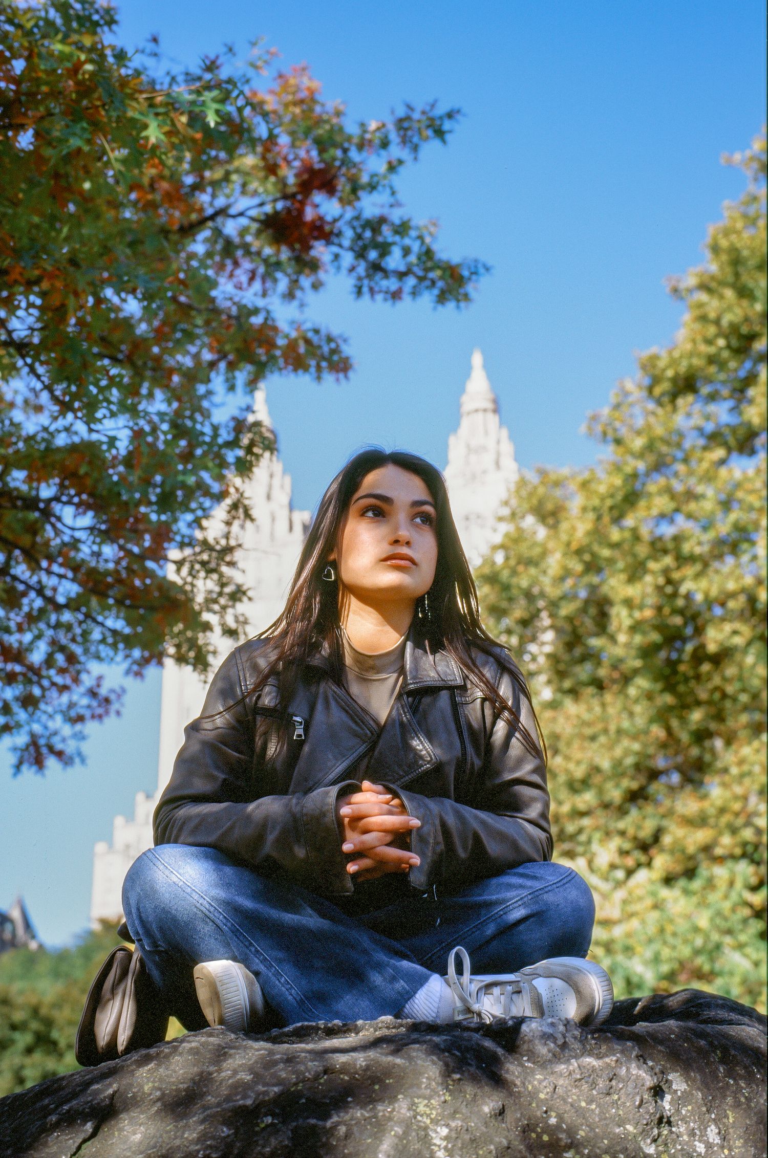 Individual sitting cross-legged on a rock with white spires visible against blue sky and fall foliage.