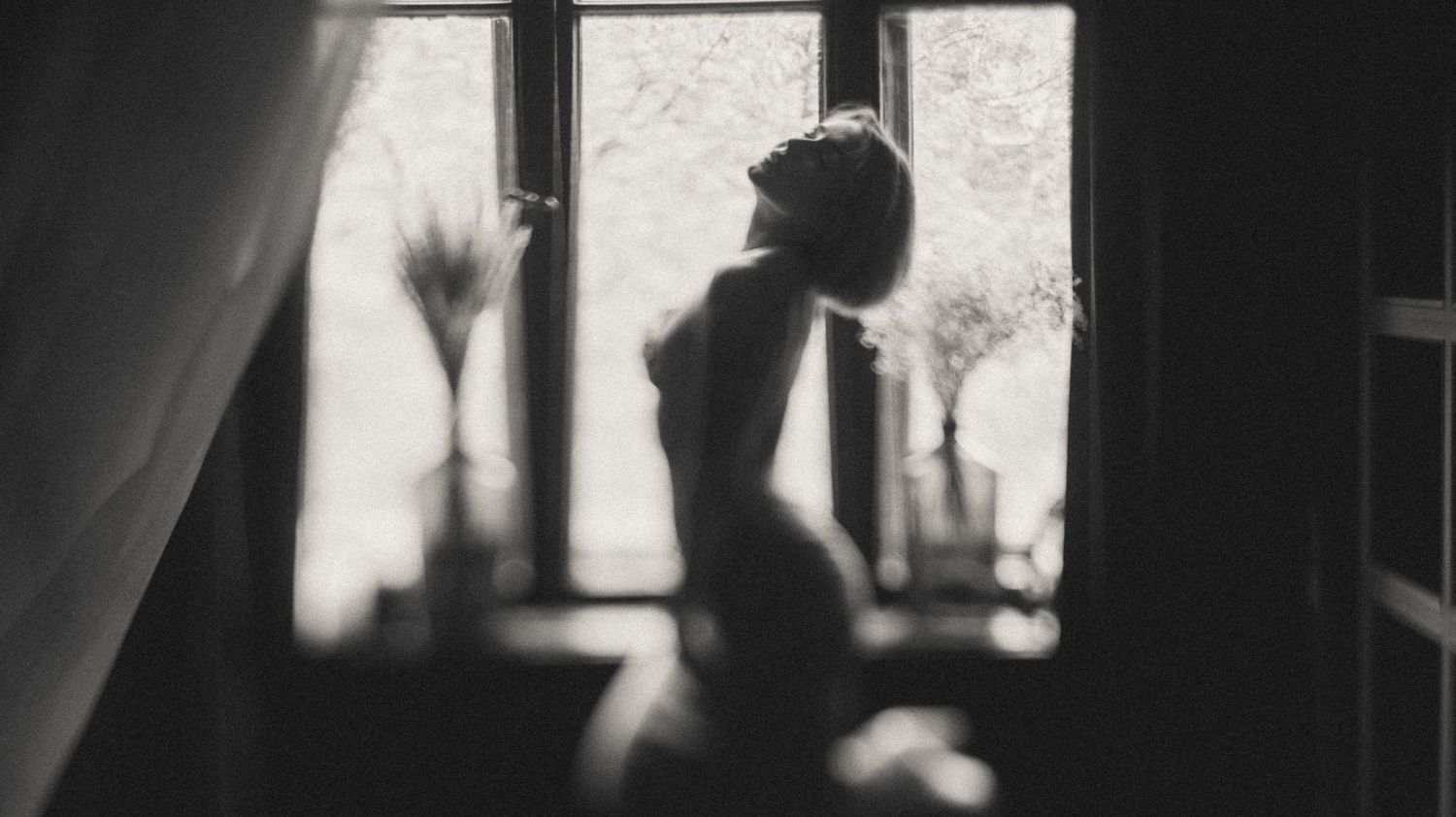 Black and white boudoir photo – artistic silhouette of a topless woman by the window