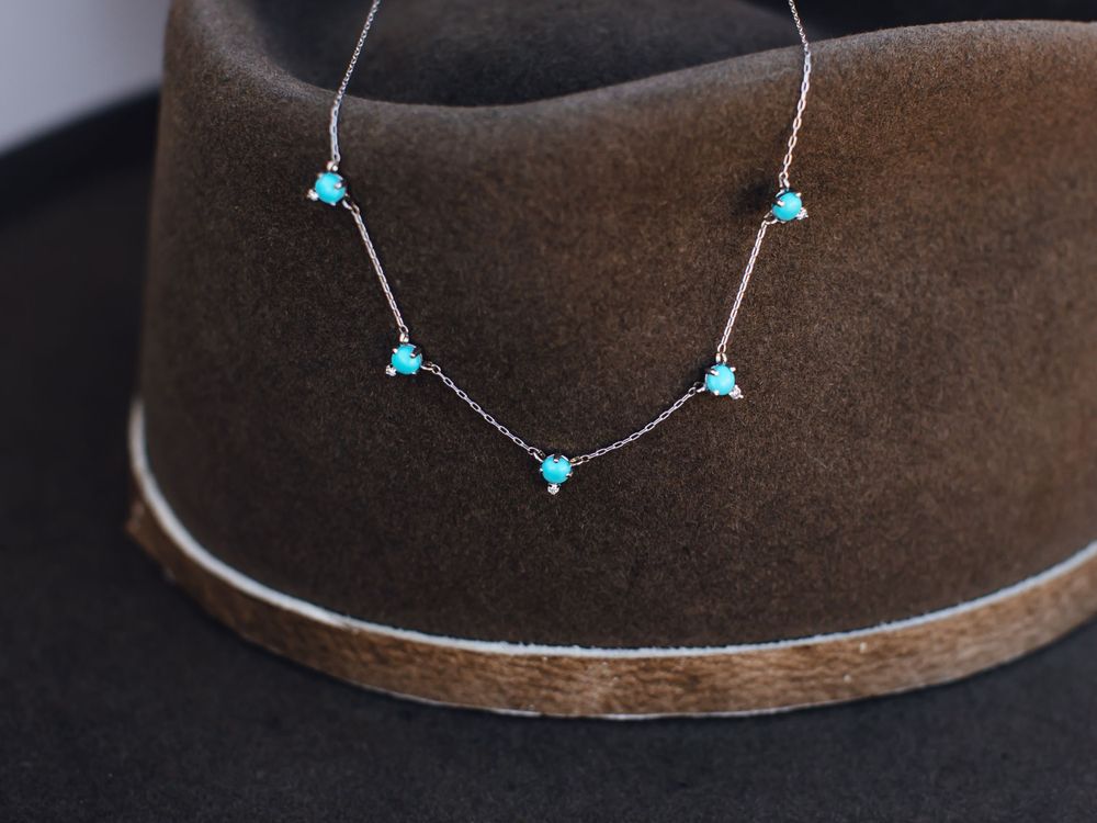 Delicate turquoise star necklace displayed on brown cowboy hat.