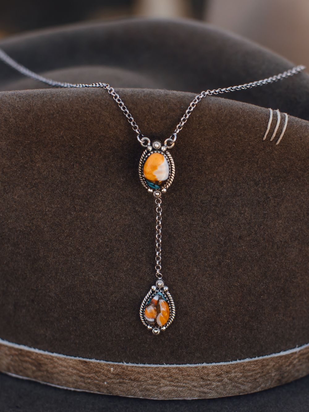 Vintage silver necklace with amber stones on brown cowboy hat displaying western style jewelry.