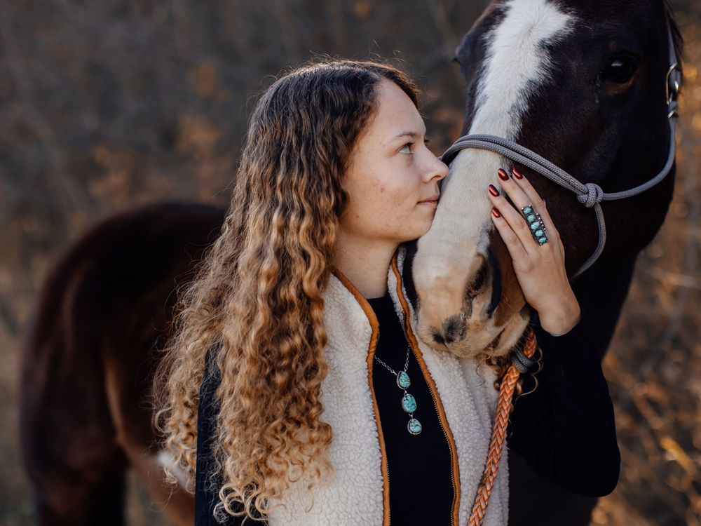 Close up of a black horse with turquoise jewelry in a rustic outdoor setting.