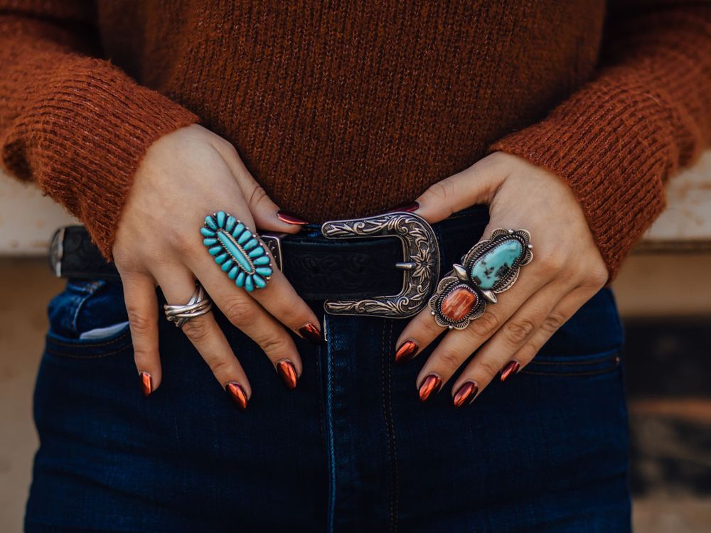 Hands showing turquoise jewelry and western-style belt buckle against denim.