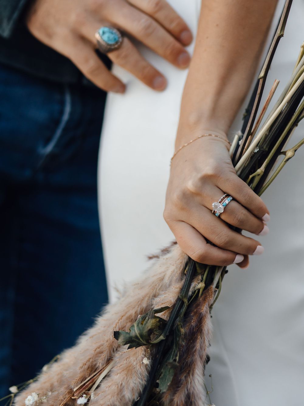 Hands holding dried flowers with turquoise and diamond rings.