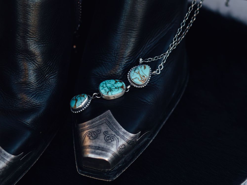Three-stone turquoise necklace displayed on black leather surface.