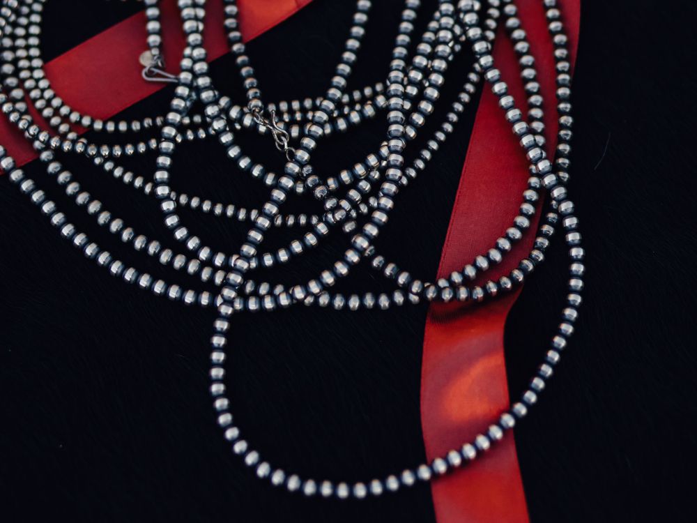 Silver beaded necklace strands arranged on black and red background.