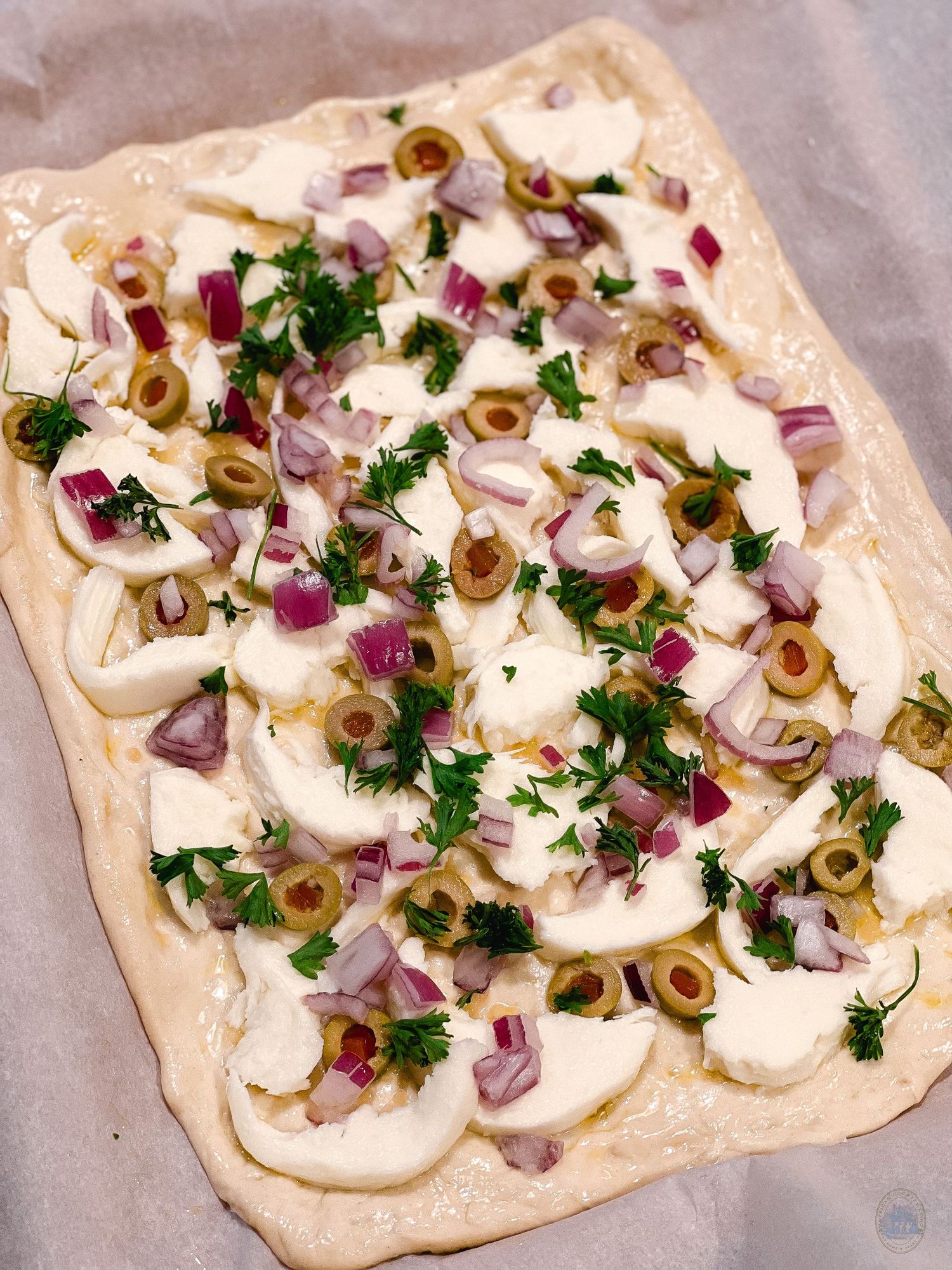 Flatbread topped with sliced mushrooms, red onions, olives and fresh herbs arranged in a progression.
