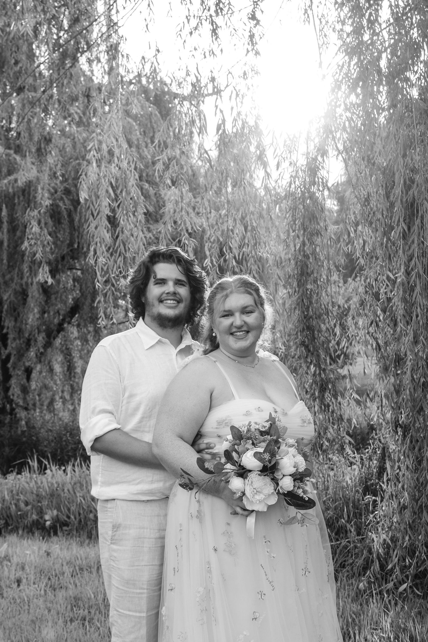 a newlywed couple standing in front of a weeping willow