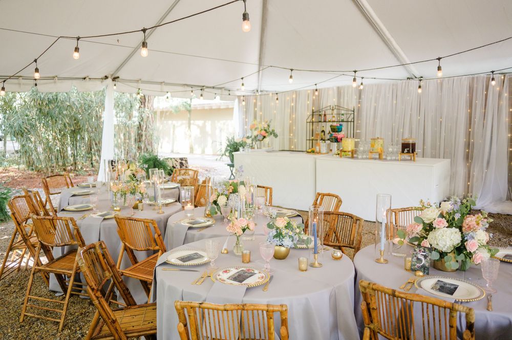 A rustic wedding reception venue decorated with string lights and round tables set with white linens and wooden chairs.
