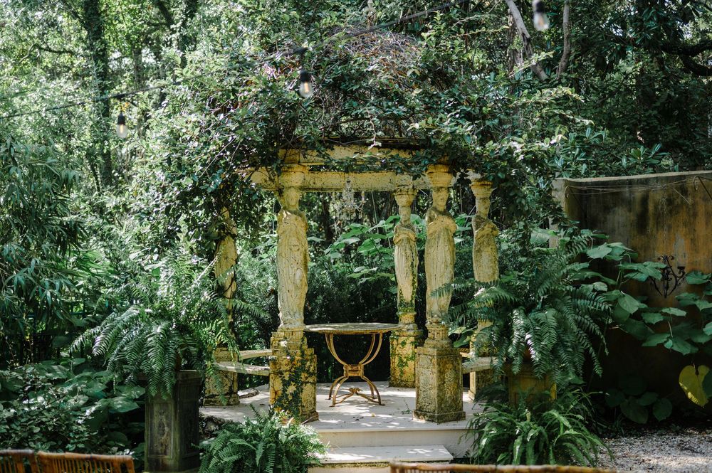 A romantic garden gazebo surrounded by lush greenery and stone columns creates an enchanting wedding venue setting.