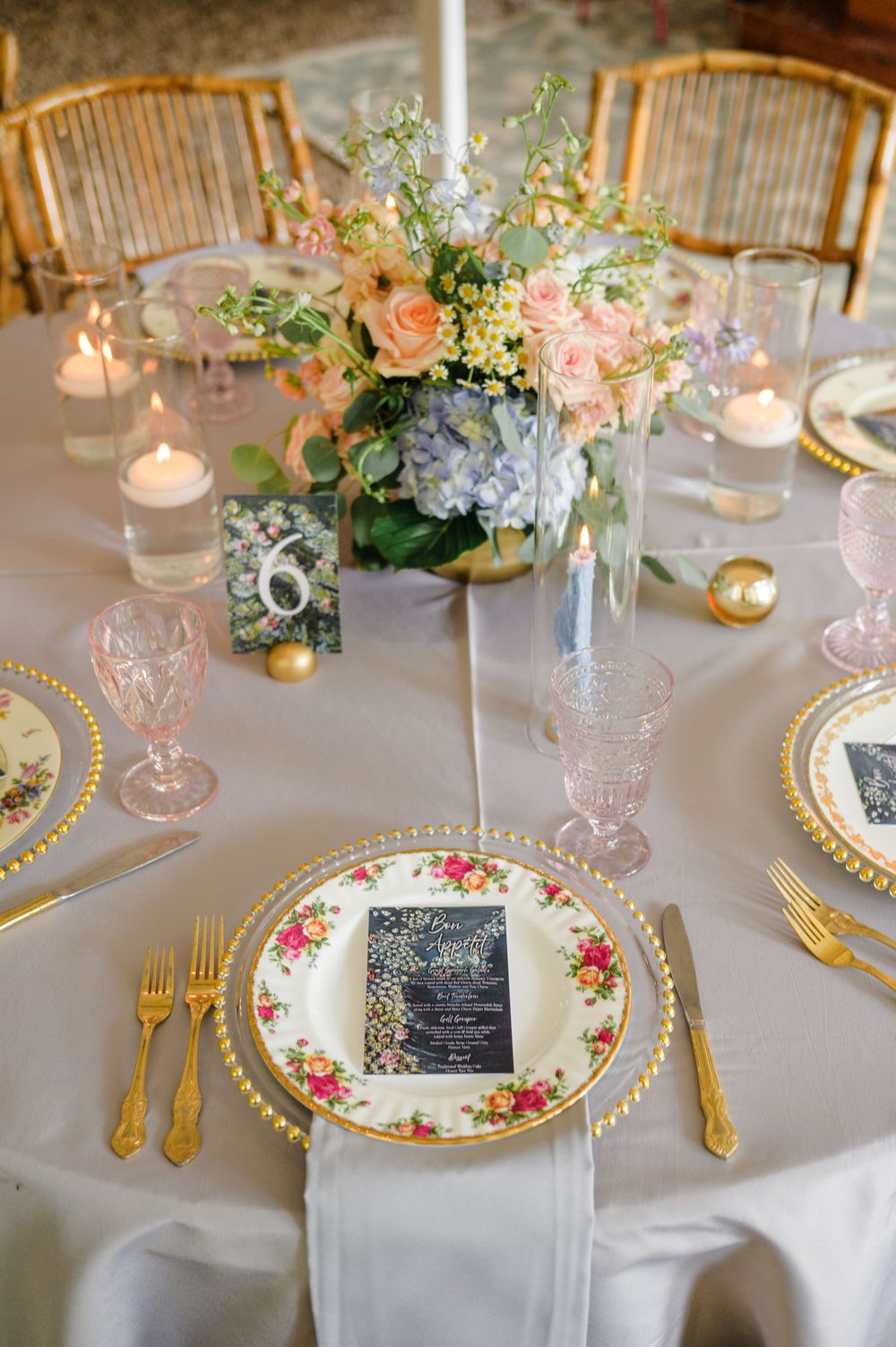 Wedding place settings featuring vintage floral plates, gold cutlery, and navy menu cards.