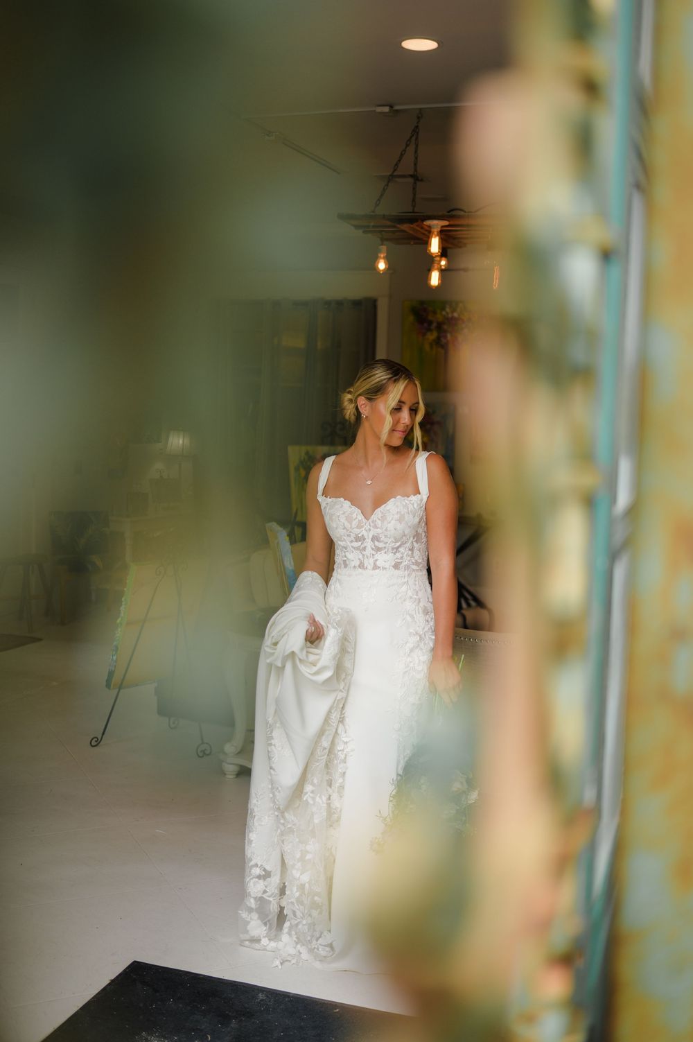 Wedding dress with lace detailing seen through a soft-focused frame with hanging pendant lights.