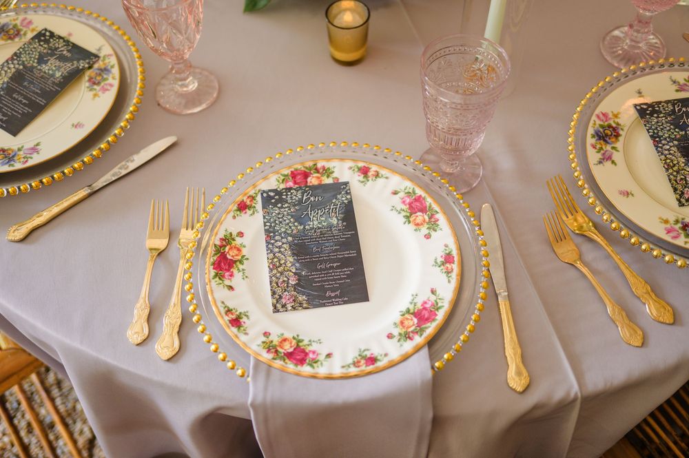 Elegant table setting with gold flatware, floral china plates, and blue menu cards at a formal event.