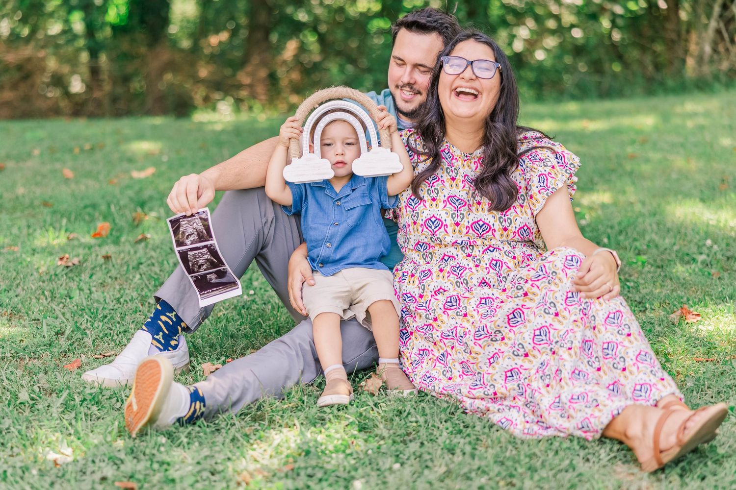 A cheerful family relaxes together on grass in a sunny outdoor setting.