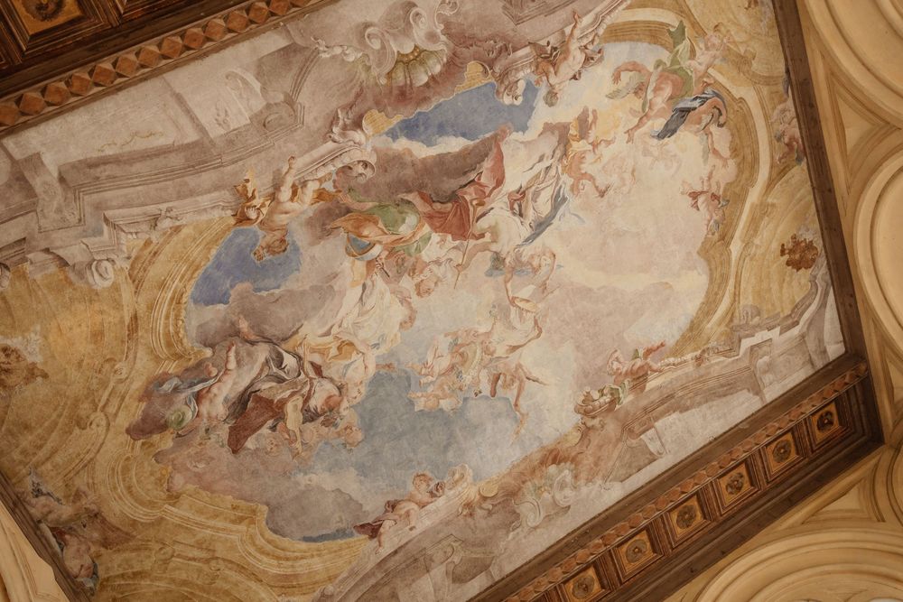 Ornate baroque ceiling fresco with religious figures and cherubs painted in soft blues and golds within an ornamental frame.