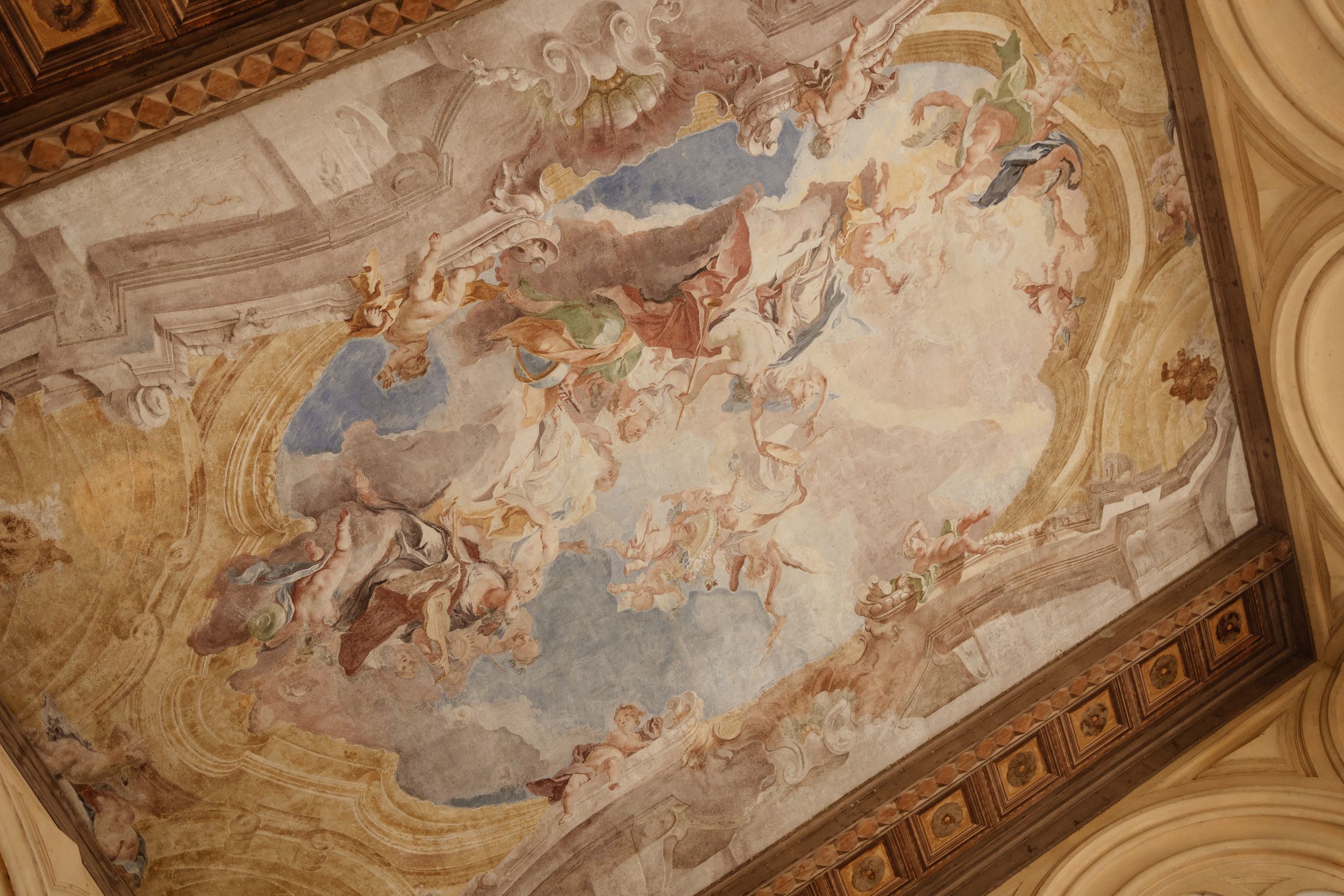 Ornate baroque ceiling fresco with religious figures and cherubs painted in soft blues and golds within an ornamental frame.