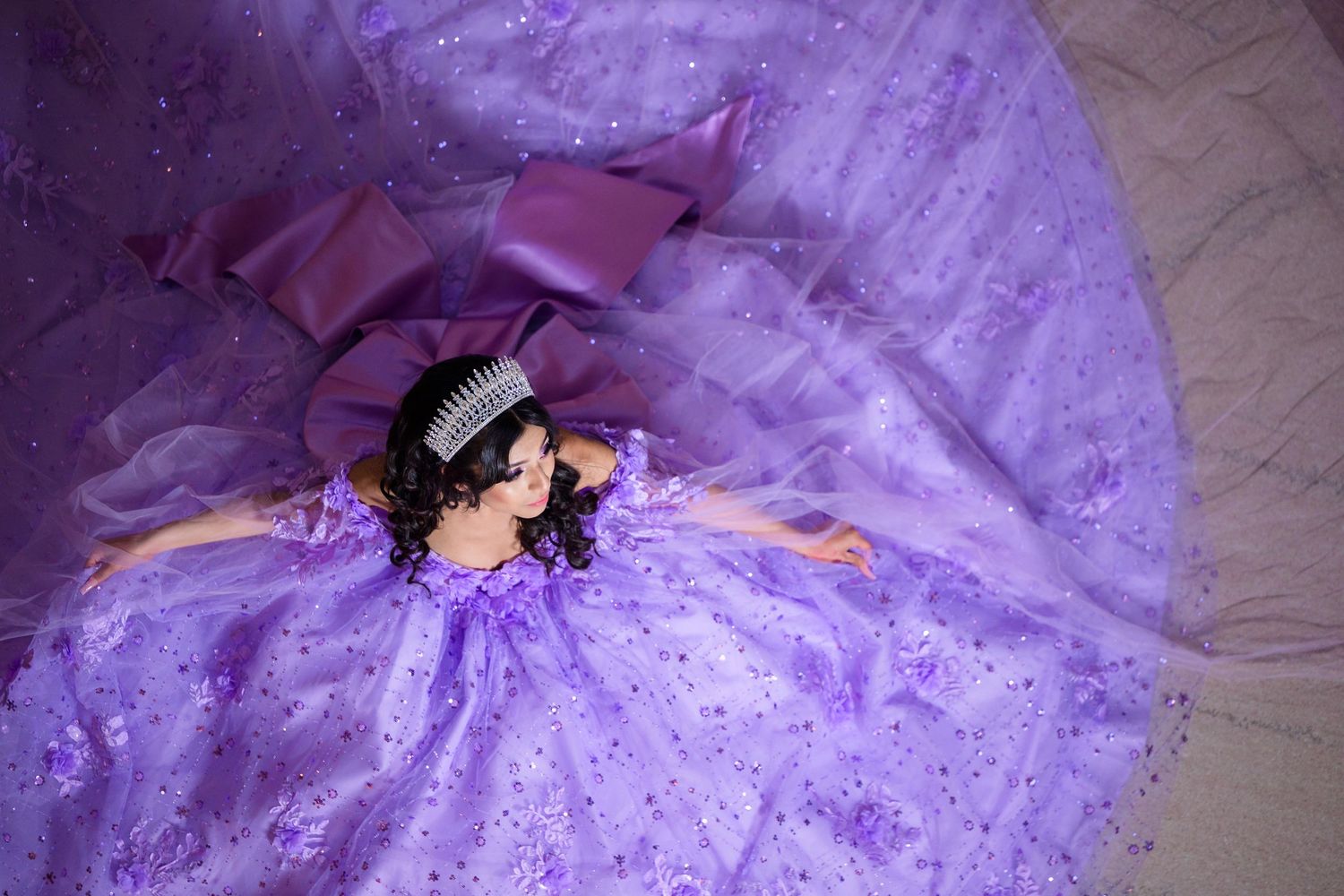 A person wearing a purple sparkly ball gown lies surrounded by tulle fabric creating a dreamy overhead view.