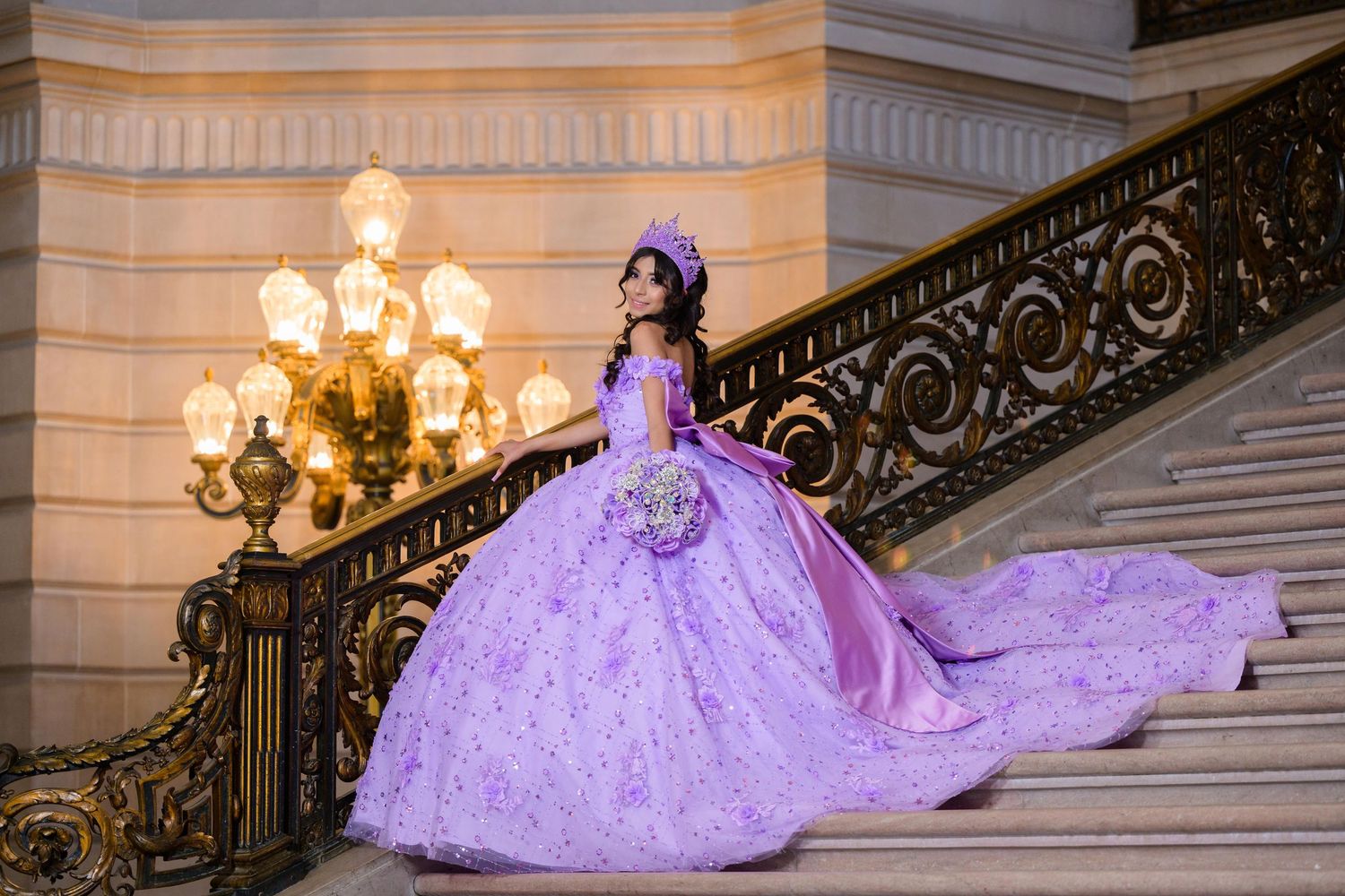 A lavish purple quinceañera gown with flowing train on an ornate staircase with golden chandelier lighting.