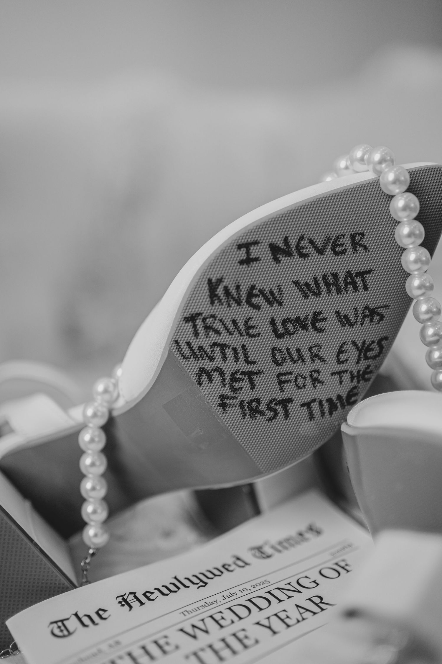A love note written on a pair of sunglasses beside pearls and a newspaper wedding announcement, captured in black and white.