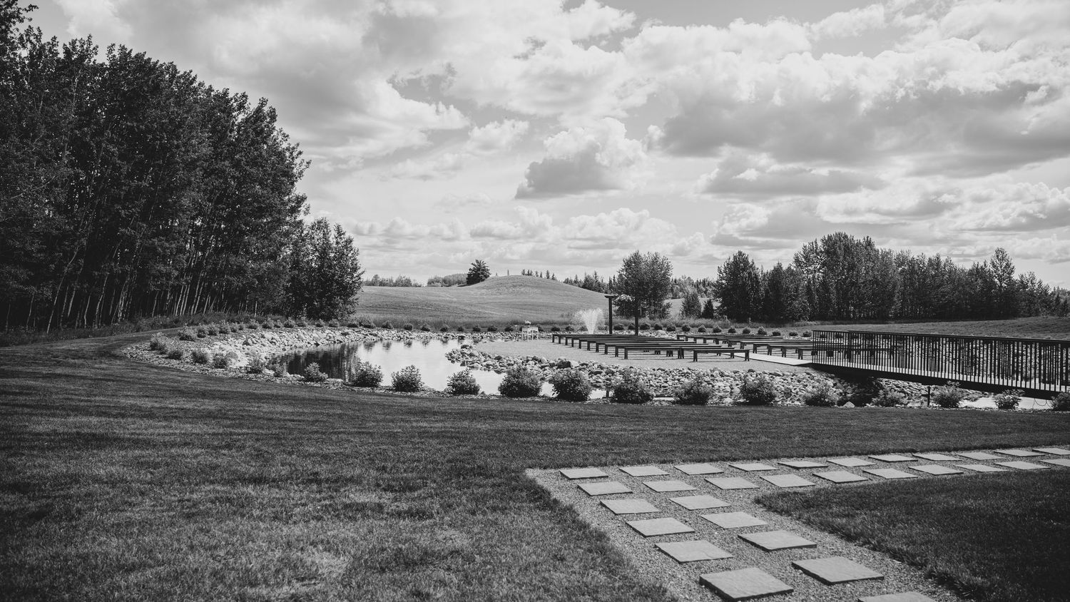 A panoramic black and white view of farmland with trees, barns and farm buildings stretching across the horizon.