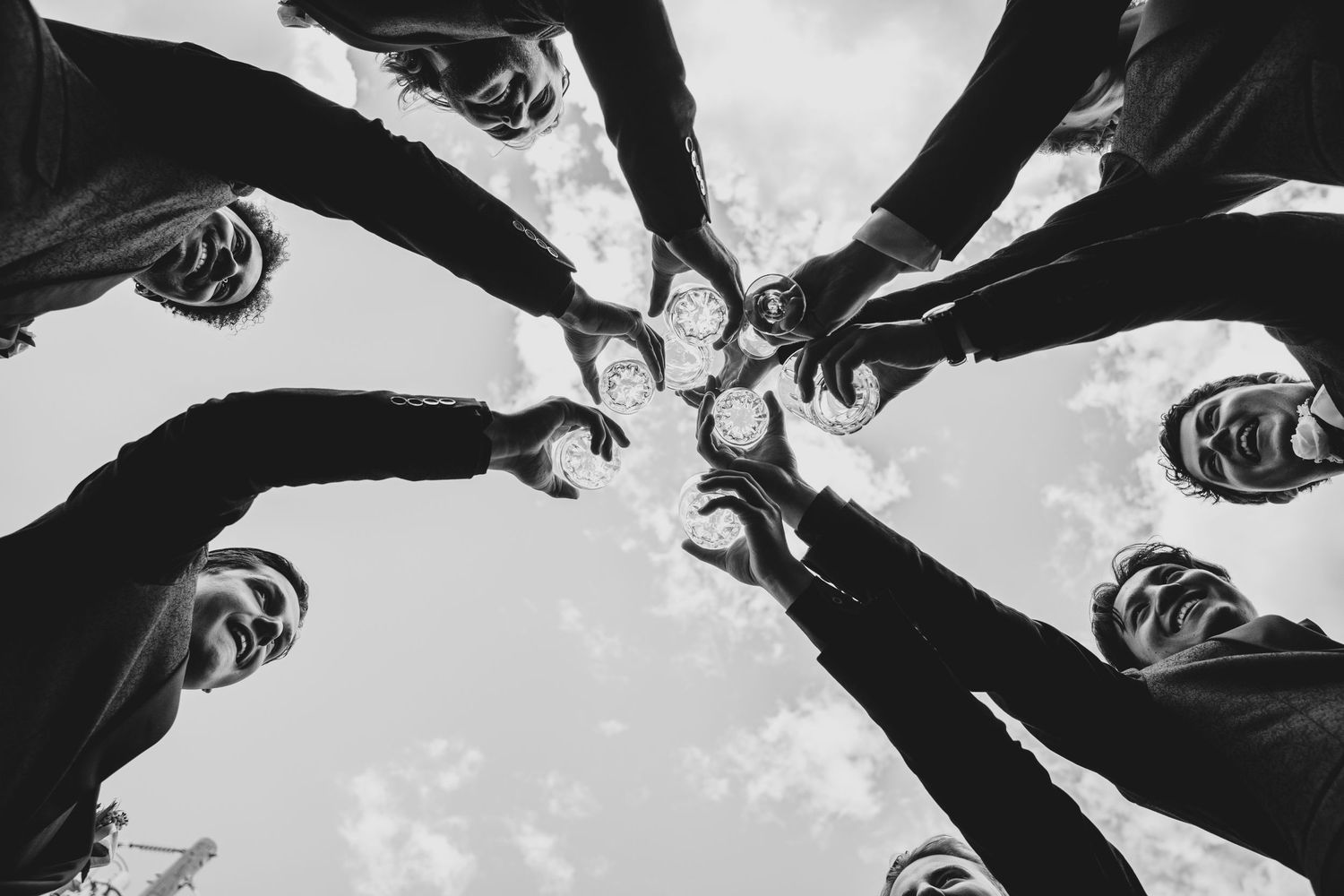 Black and white artistic photo of people looking down at the camera in a circular formation against a gray sky.