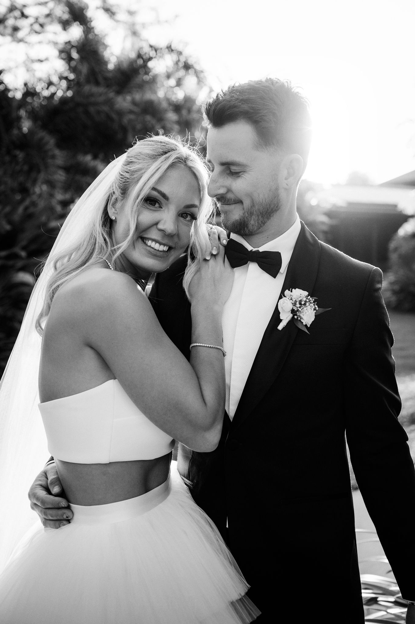 A romantic black and white wedding portrait of a couple embracing outdoors in formal attire.
