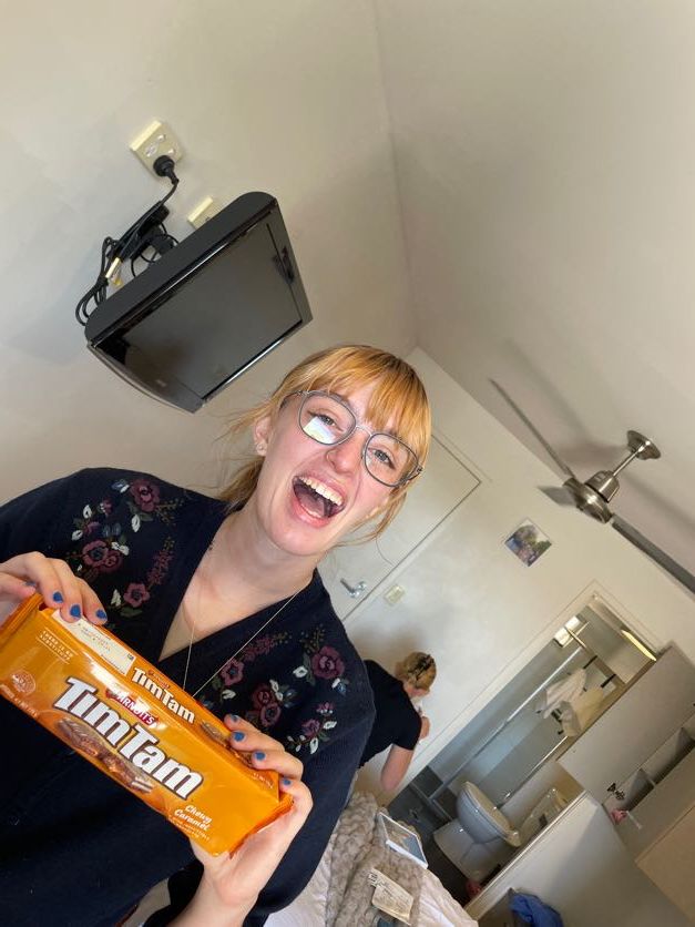 Person holding and displaying an orange Tim Tam cookie package with enthusiasm.