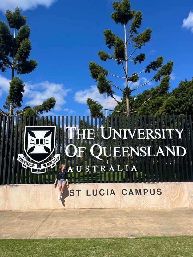 The University of Queensland St Lucia campus entrance sign with blue sky and trees.