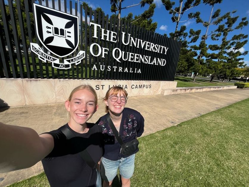 University of Queensland campus entrance sign surrounded by trees on a sunny day.