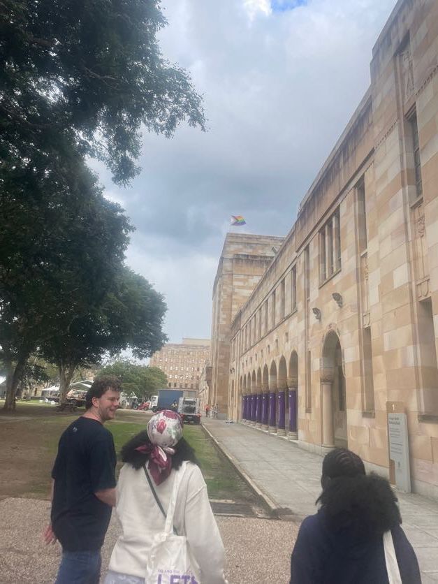 Group walking along sandstone university building exterior path under cloudy sky.