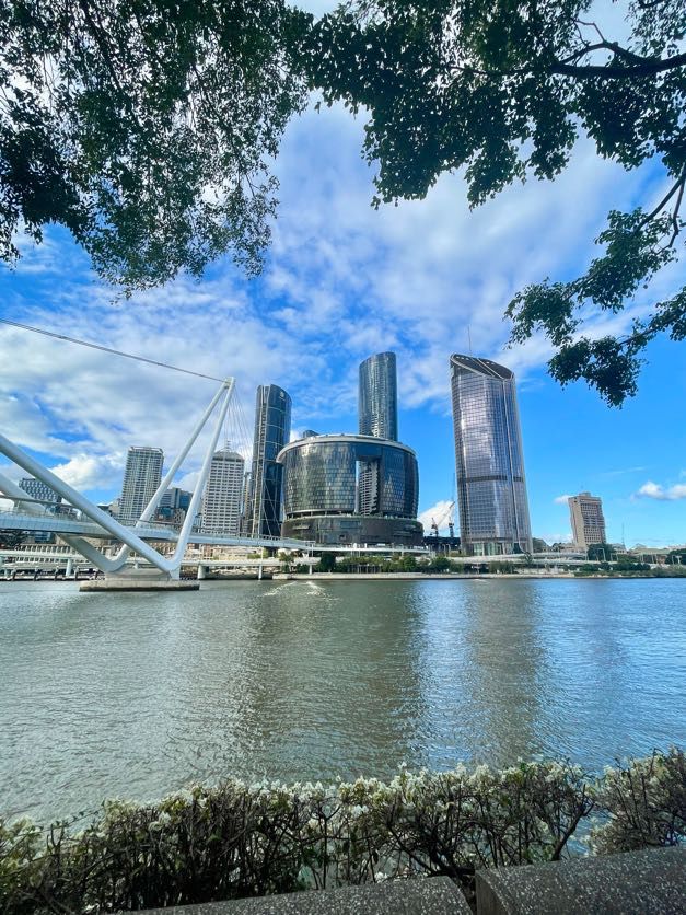 Brisbane River waterfront with modern skyscrapers and blue sky reflecting on the water.