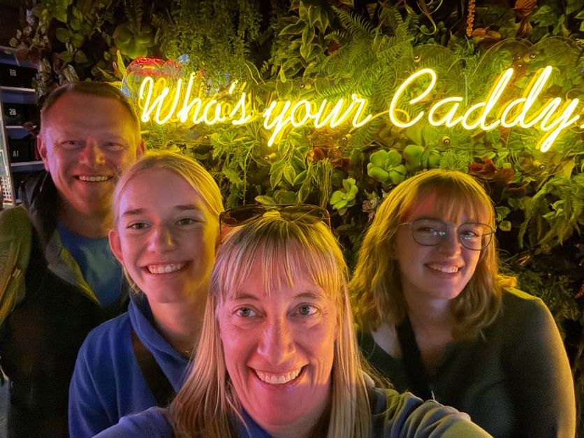 Friends posing together under illuminated yellow neon signage at night.