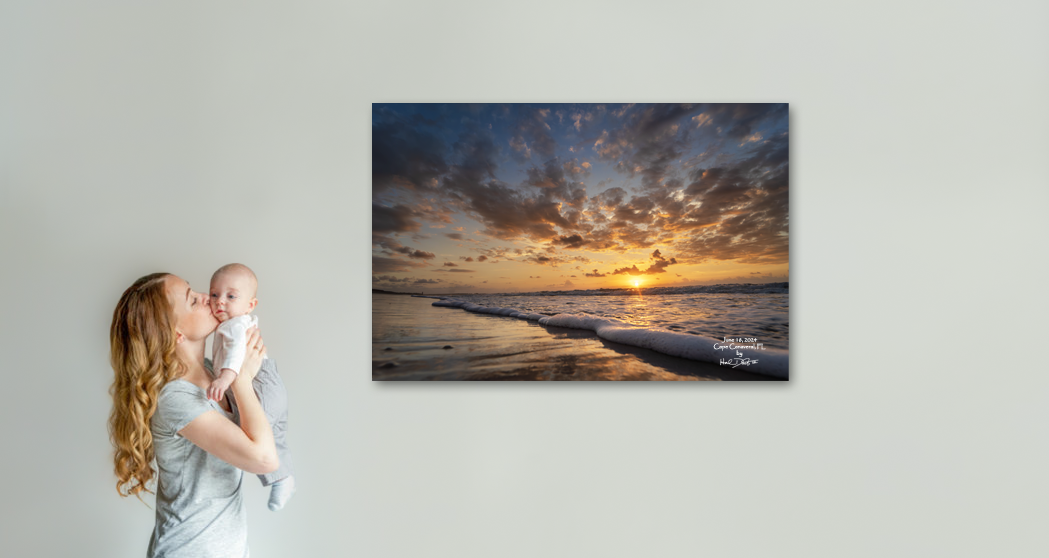 Beautiful coastal sunrise artwork displayed on wall while new mother kisses her newborn baby at home. Image has the date of the babies birth