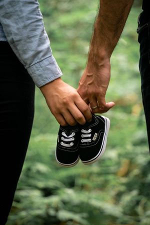 Hands hold a small pair of black baby shoes against a green natural background.