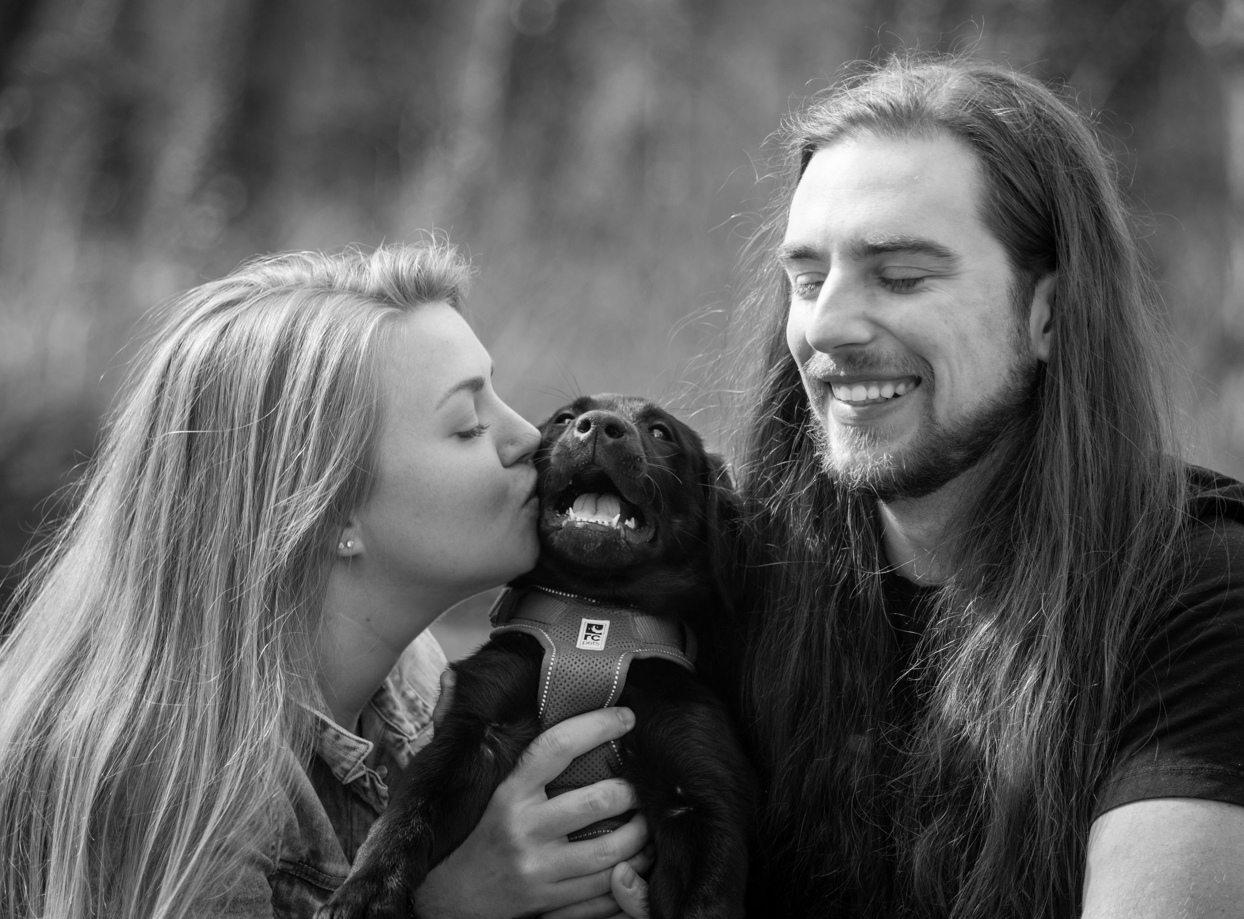 A couple sharing a joyful moment with their black dog in a candid black and white portrait.